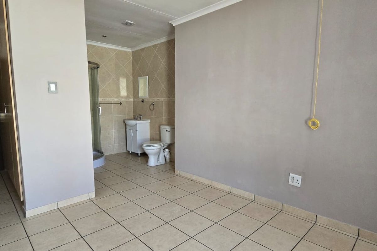 A spacious bedroom featuring tiled flooring, built-in cupboards, and an attached en-suite bathroom with a shower, basin, and toilet.
