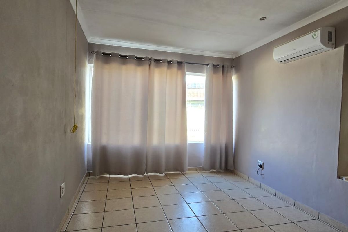 An empty living room featuring tiled flooring, a wall-mounted air conditioning unit, and a decorative glass block window feature.