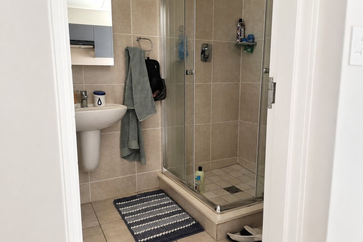A functional bathroom featuring a pedestal basin, tiled walls, and a glass-enclosed shower unit.