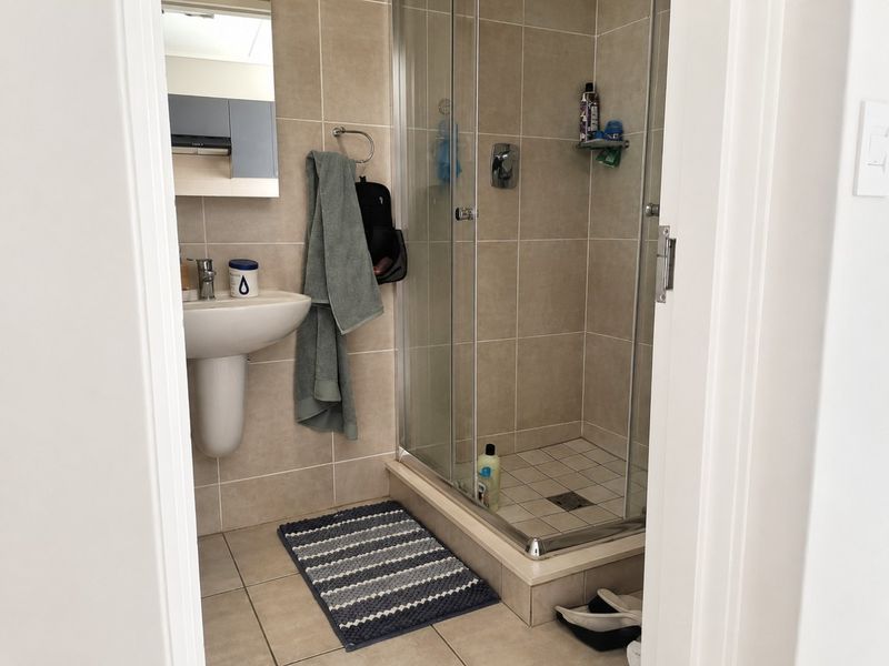 A functional bathroom featuring a pedestal basin, tiled walls, and a glass-enclosed shower unit.