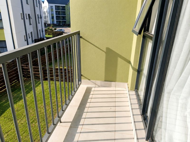 A clean, private balcony featuring tiled flooring and a metal balustrade, overlooking the surrounding apartment complex grounds.