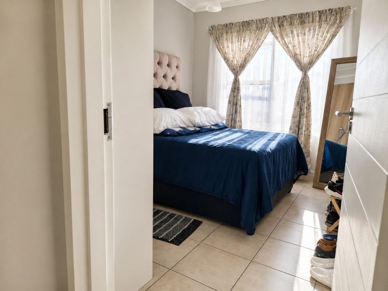 A well-lit bedroom featuring neutral tiled flooring and large windows with curtain rails, offering a comfortable and functional living space.