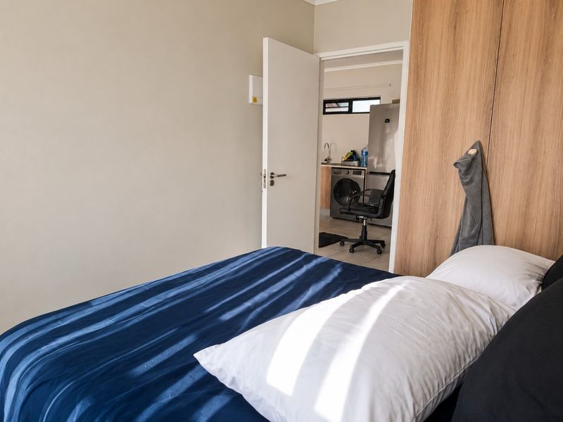 A bedroom featuring a built-in wardrobe with wood-grain finish, offering a view into the adjacent kitchen area.