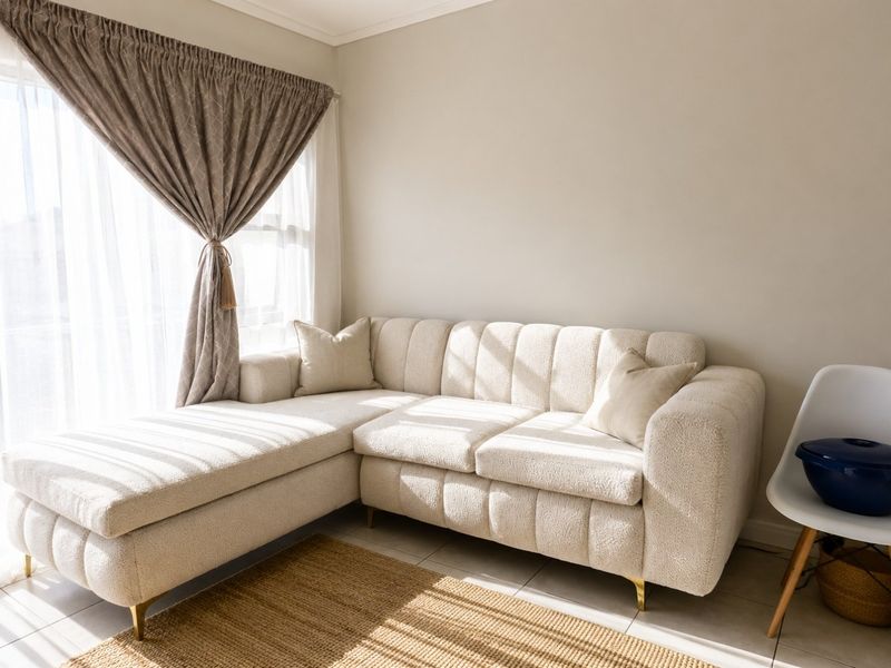 A bright and inviting living room area featuring neutral tiled flooring and natural light streaming through a large window with installed curtain tracks.