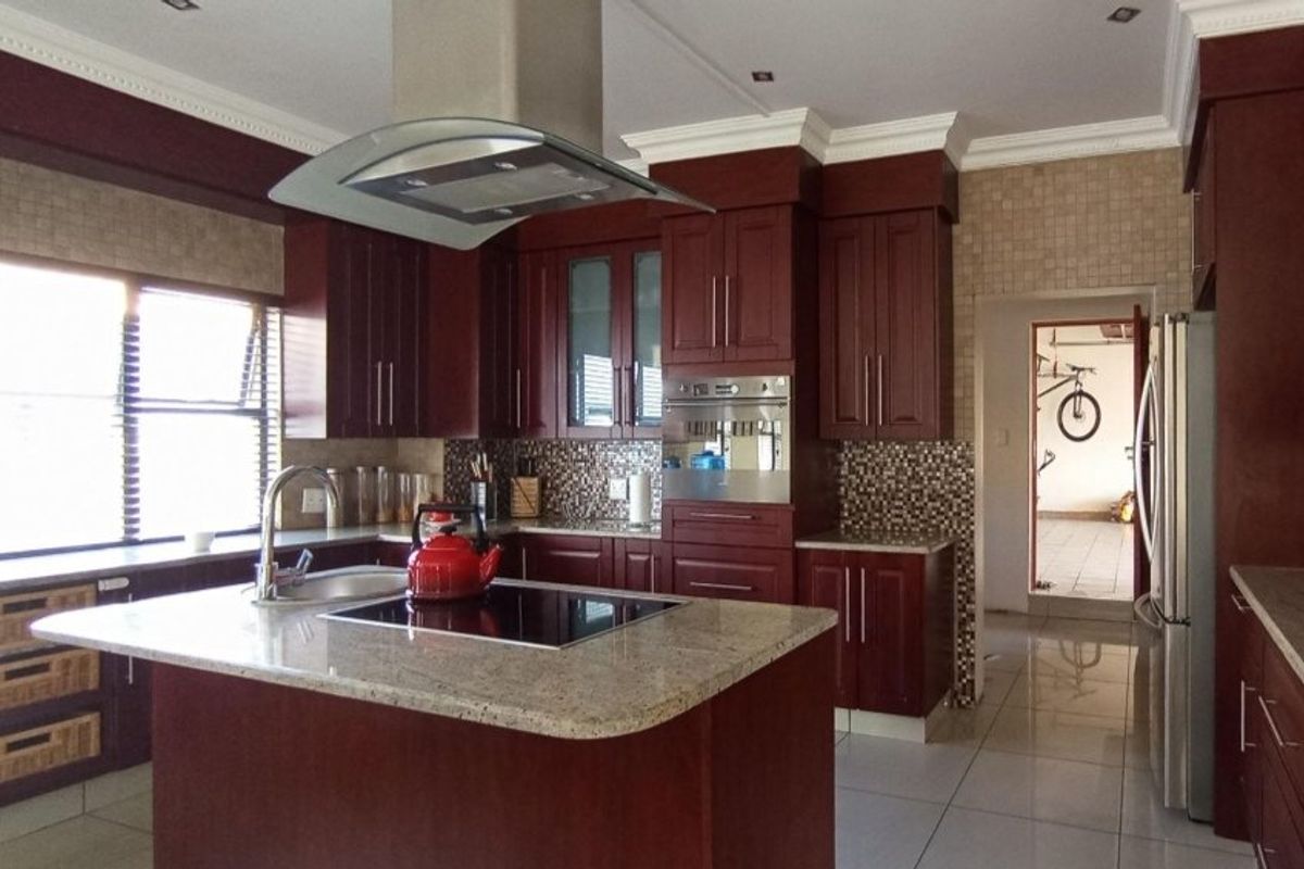 Spacious kitchen featuring dark wood cabinetry, granite countertops, a central island with an integrated hob, and a modern extractor fan.
