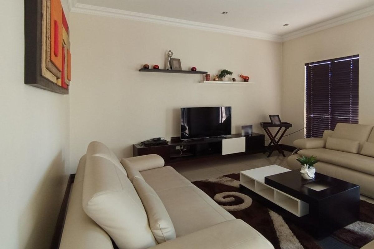A well-maintained living room featuring tiled flooring, recessed downlighting, crown molding, and venetian blinds, providing a comfortable and neutral space.