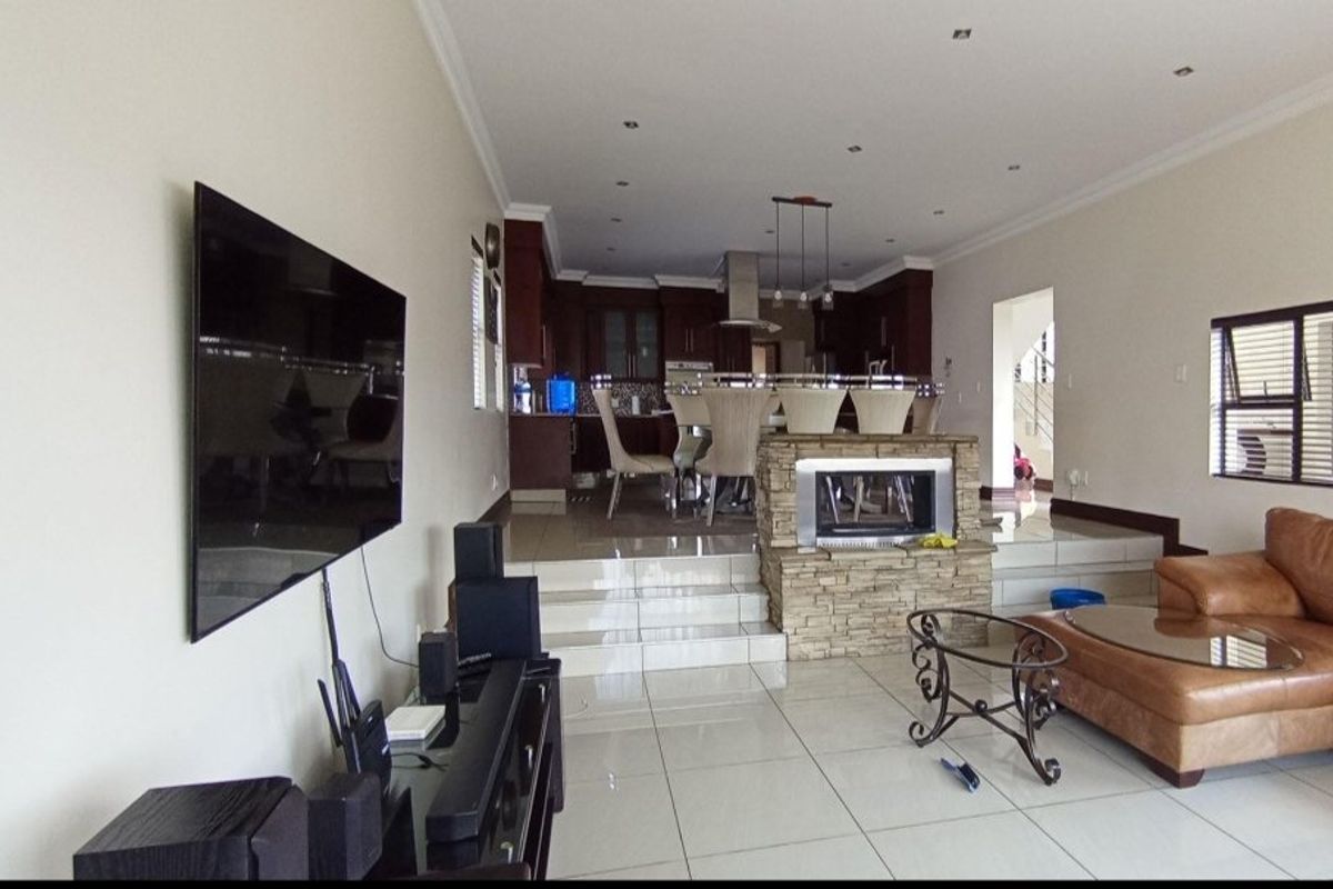 Open-plan living and kitchen area featuring a raised platform, stone-clad fireplace, tiled flooring, and dark wood cabinetry.