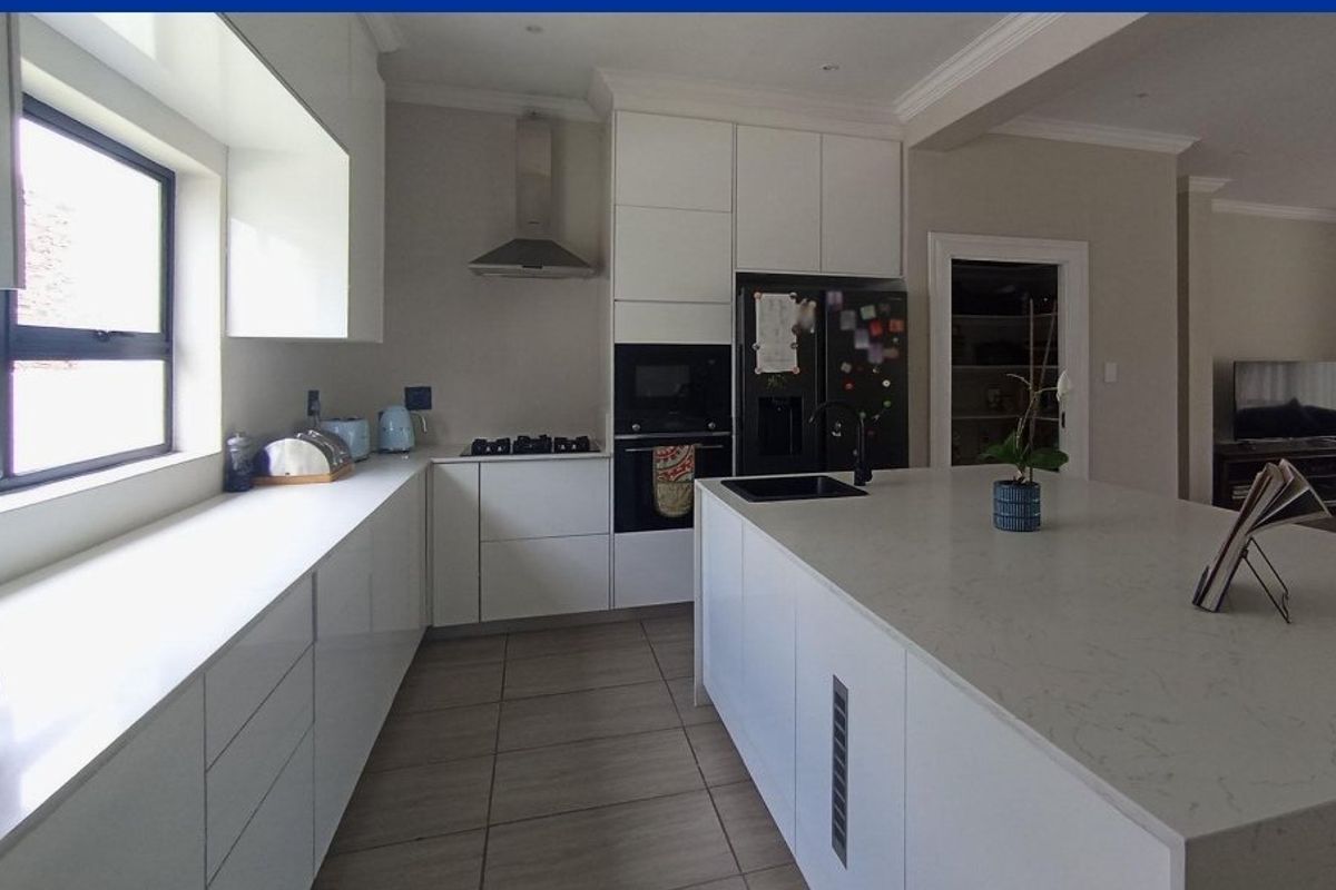 Modern kitchen featuring a large central island with stone countertops, built-in appliances, sleek white cabinetry, and tiled flooring.