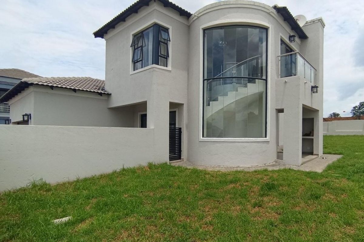 Rear view of a modern double-story house featuring a prominent curved glass facade, internal staircase, and a private balcony.