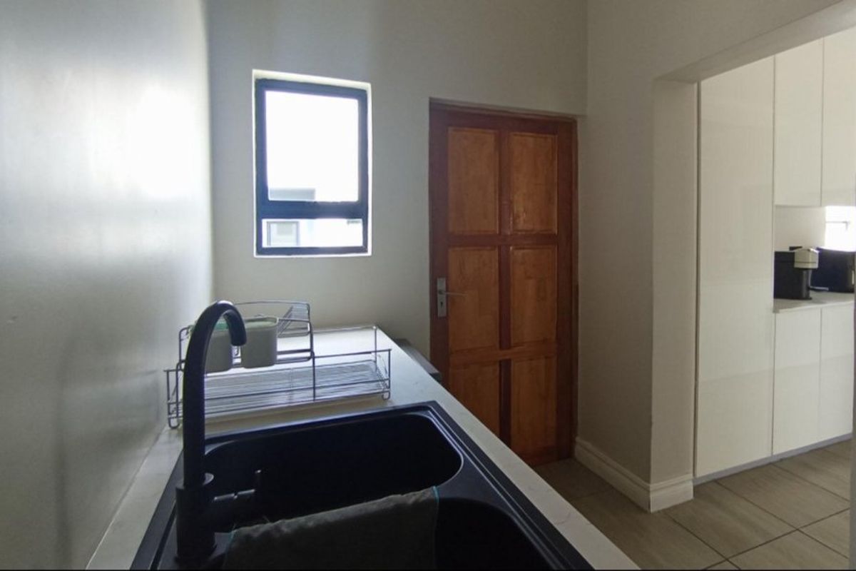 A functional scullery area featuring a double sink with a modern black mixer tap, tiled flooring, and a solid timber door.