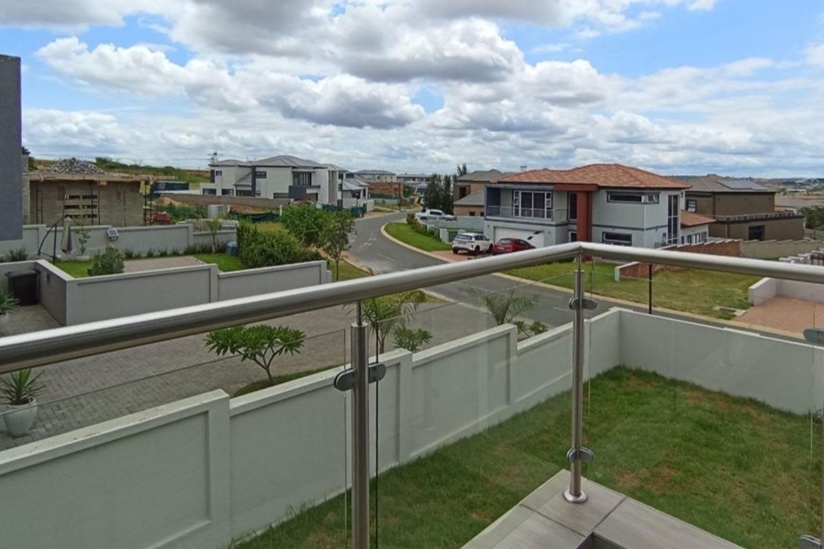 An elevated balcony featuring a modern stainless steel and glass balustrade, offering an open view of the surrounding residential estate.