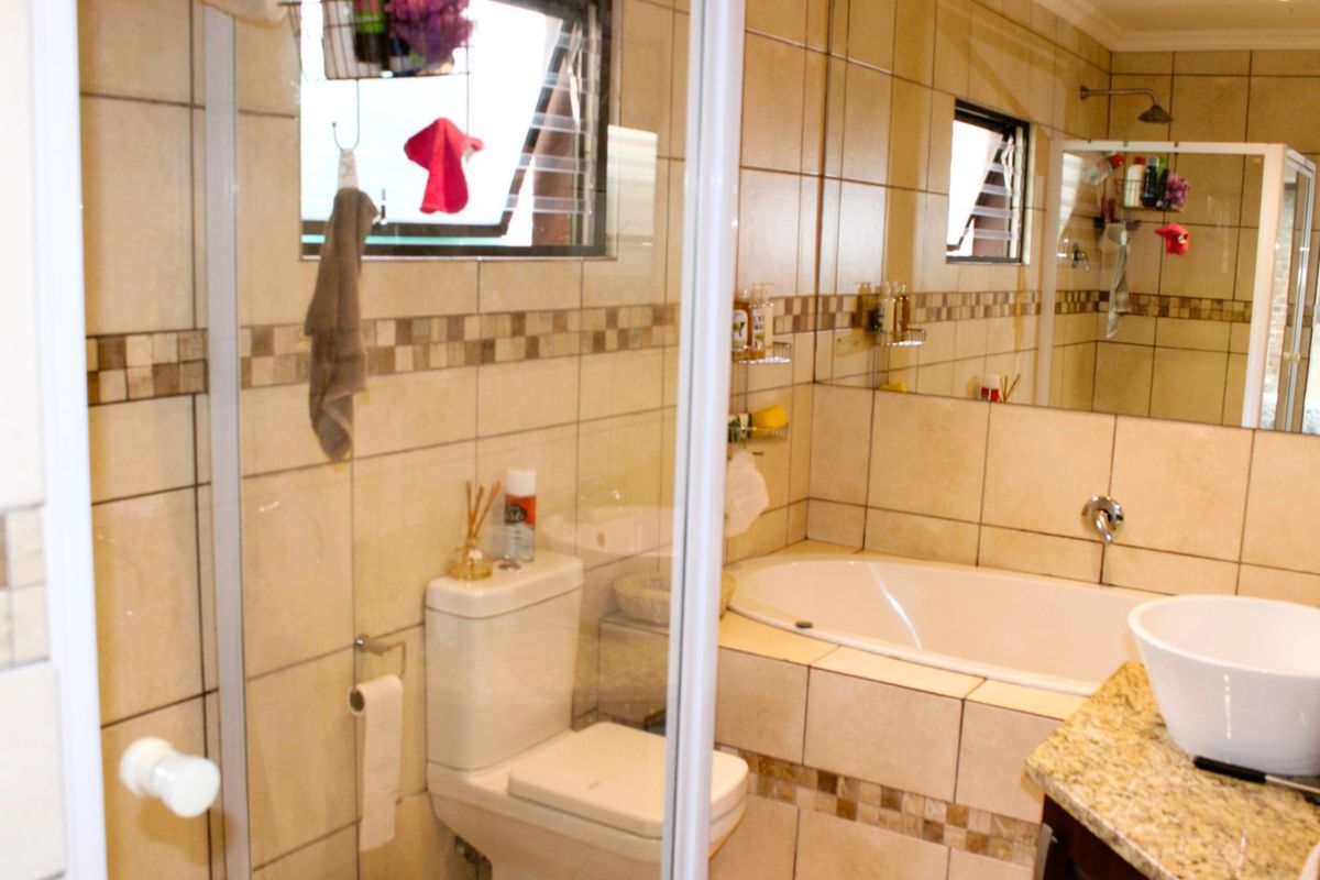 A functional bathroom featuring a shower enclosure, built-in bathtub, toilet, and a vessel sink set on a granite vanity countertop with tiled walls.