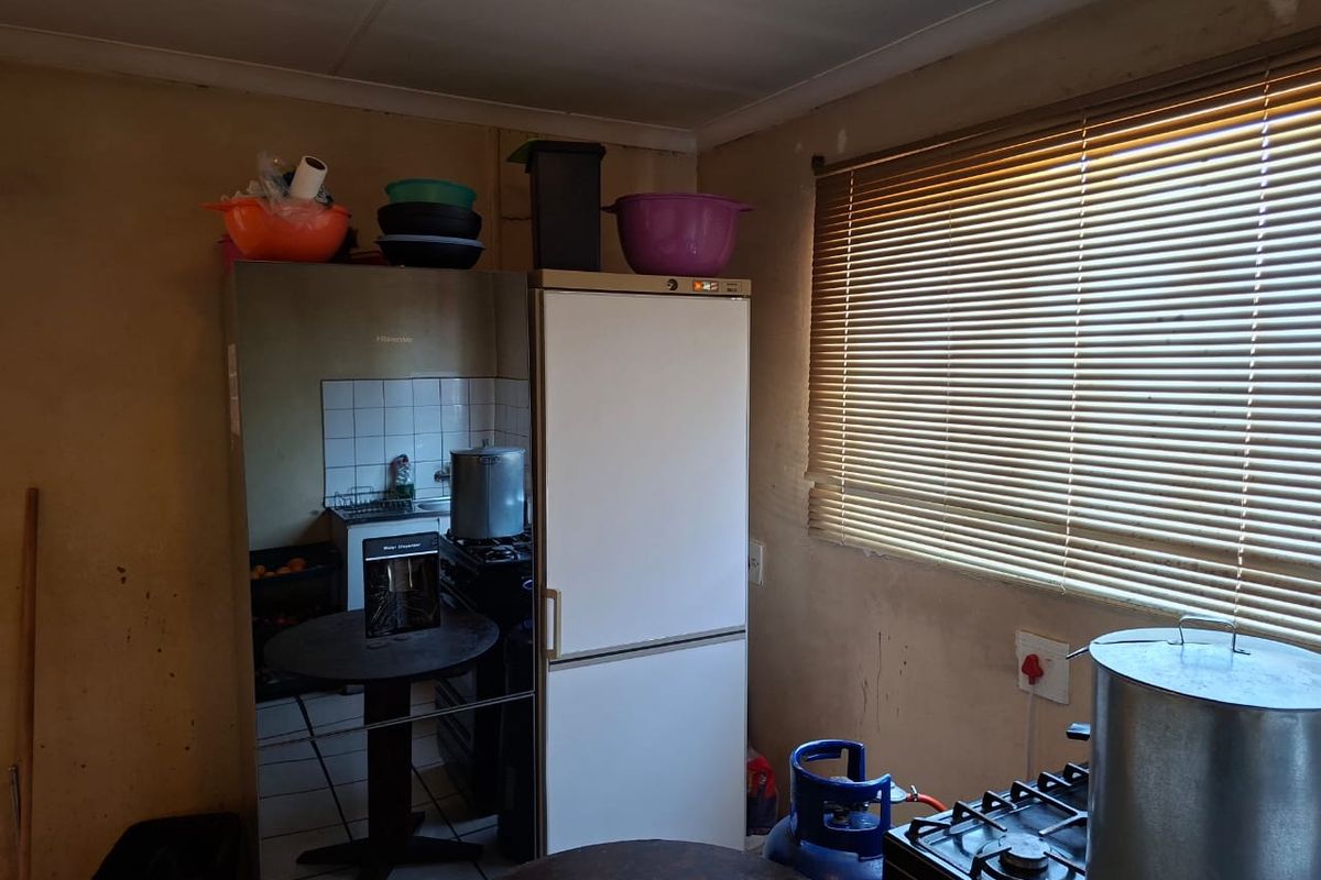 A dated kitchen area featuring a gas hob, tiled splashback, and venetian blinds, requiring cosmetic updates and wall refinishing.