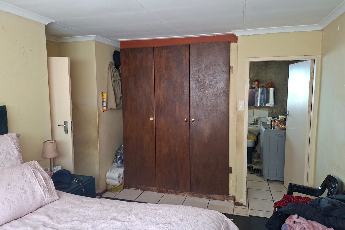 Bedroom featuring built-in wooden wardrobes and tiled flooring, with an adjacent utility area visible through the doorway.