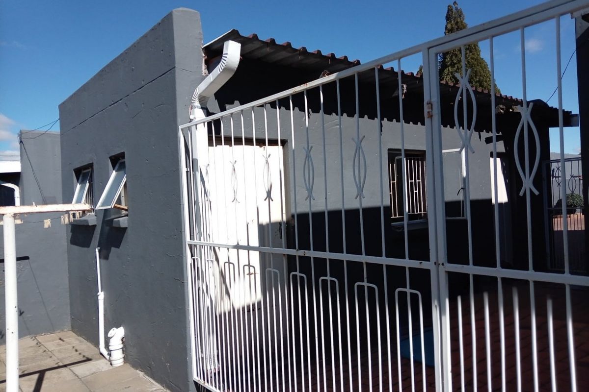 Rear exterior view of the apartment featuring a paved patio area, metal security gate, and corrugated roofing.