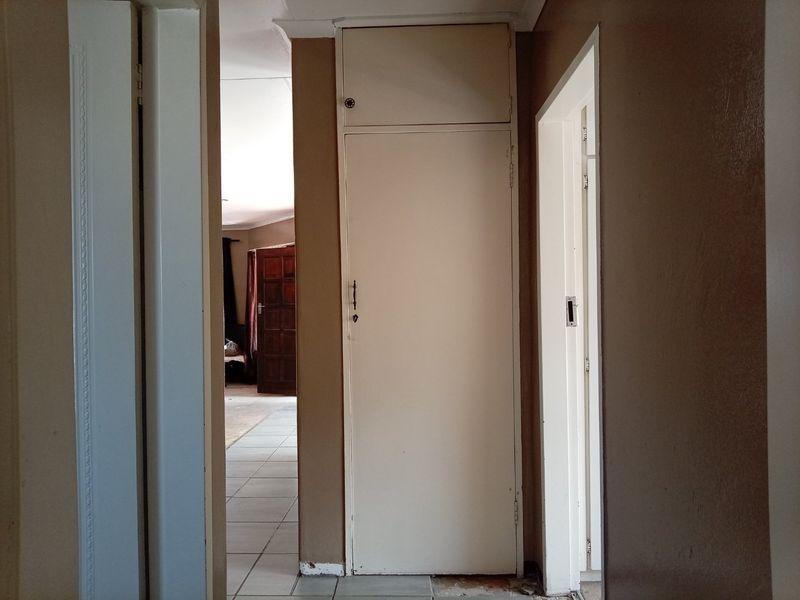 A functional hallway featuring a built-in linen cupboard and tiled flooring, providing access to adjacent rooms within the apartment.