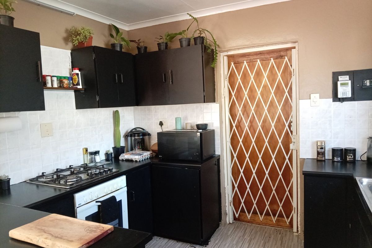 A functional kitchen featuring dark cabinetry, a gas hob, built-in oven, and a security gate leading to the exterior.