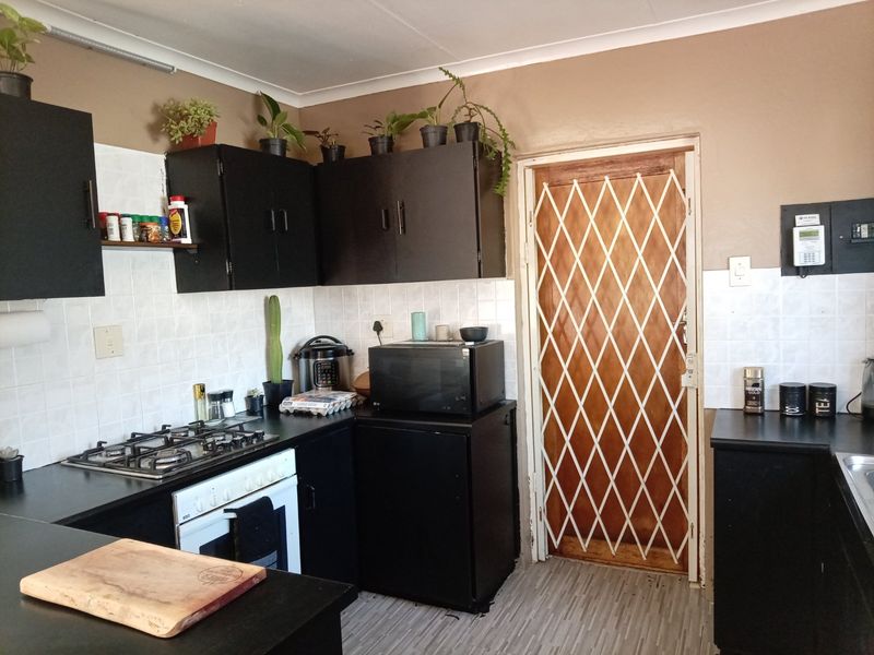 A functional kitchen featuring dark cabinetry, a gas hob, built-in oven, and a security gate leading to the exterior.