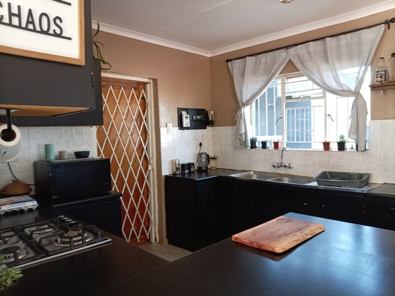 A functional kitchen featuring dark cabinetry, a gas hob, double sink, and a security gate leading to the exterior.