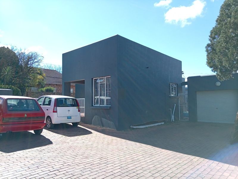 Front exterior view of the apartment building featuring a paved driveway, attached garage, and dark grey rendered facade with security bars on windows.