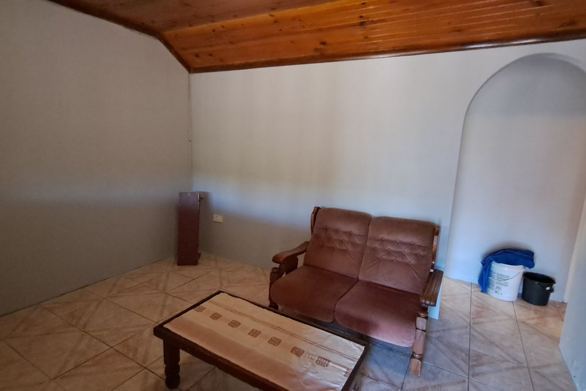 A living room featuring ceramic floor tiles, a timber-clad vaulted ceiling, and a distinctive arched doorway leading to an adjacent space.