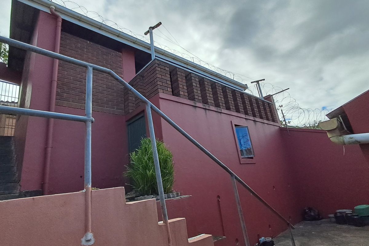Rear exterior view of the property featuring a concrete staircase, metal handrails, and perimeter security fencing with razor wire.