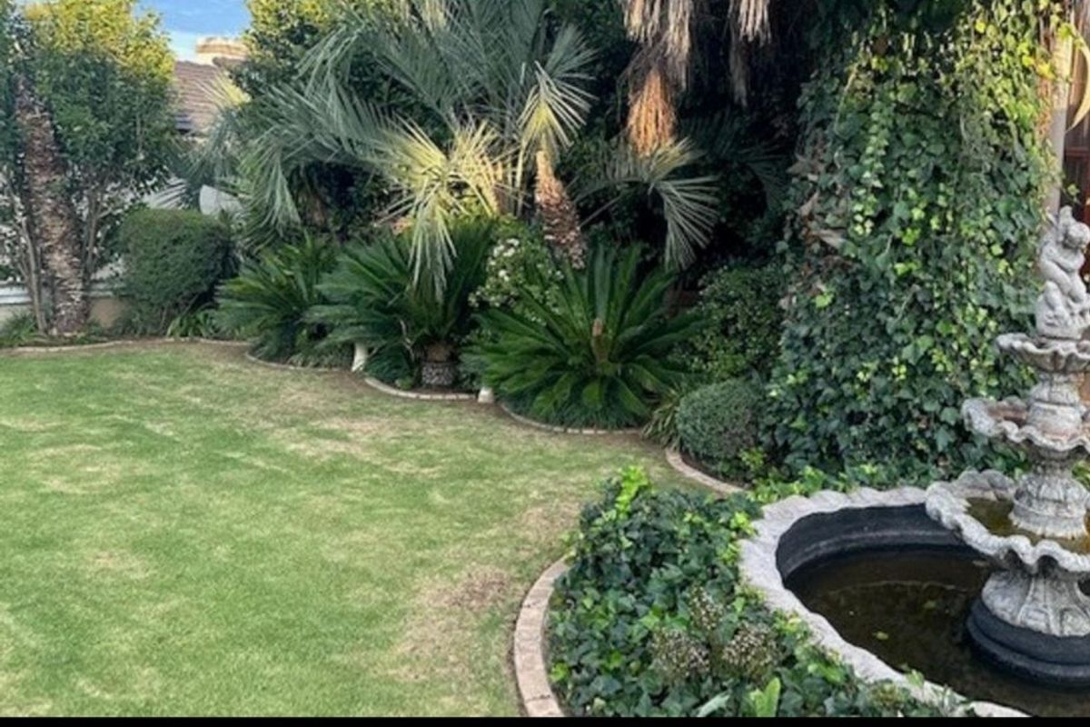 A well-established garden featuring a stone fountain, mature palm trees, and neatly edged lawn areas.