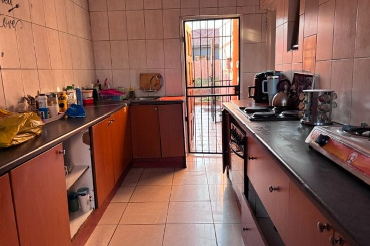 A functional kitchen featuring built-in cabinetry, laminate countertops, and tiled finishes, with direct access to the exterior through a security gate.