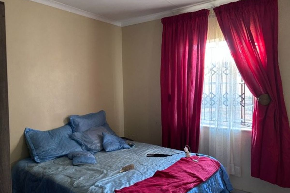 A standard bedroom featuring neutral wall finishes, coving, and a window fitted with a security gate.