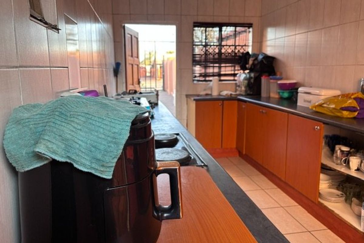 A functional kitchen featuring tiled walls, laminate cabinetry, and a built-in hob, with direct access to the exterior.
