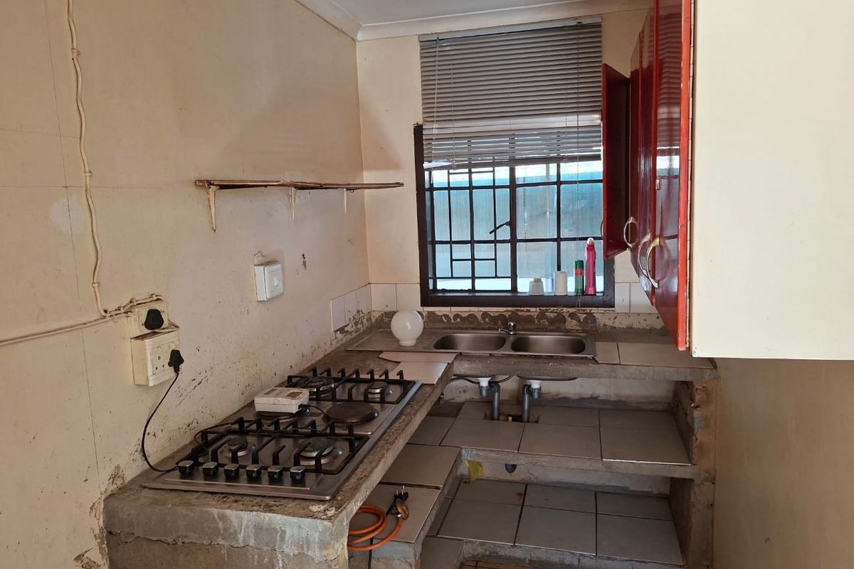 A dated kitchen featuring a gas hob, double sink, and concrete shelving, requiring significant renovation and cosmetic updates to improve functionality and aesthetic appeal.