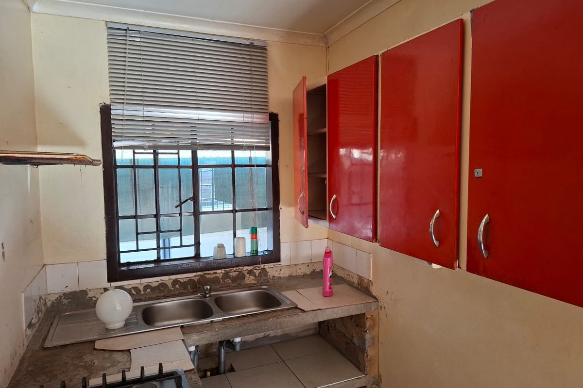 A dated kitchen featuring red cabinetry, a double bowl stainless steel sink, and a gas hob, requiring significant renovation and finishing to improve functionality.