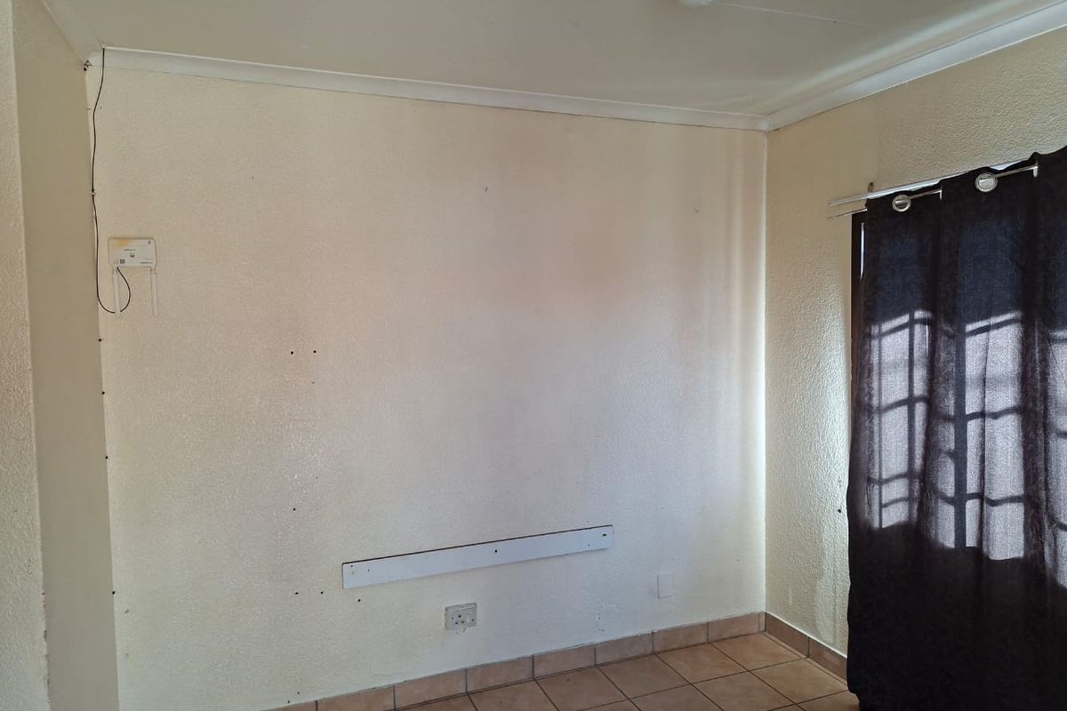 An empty bedroom featuring tiled flooring, coved ceilings, and wall-mounted fixtures, requiring minor cosmetic repairs and fresh paint to enhance its appeal.