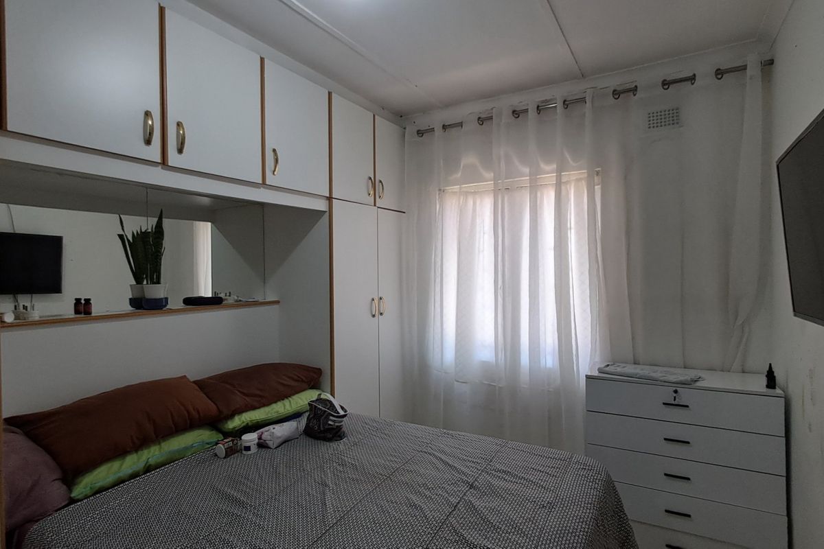A bedroom featuring extensive built-in white cabinetry with integrated mirrored shelving and a window fitted with a curtain rail.