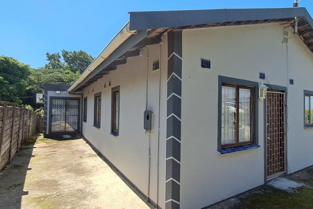 A view of the rear exterior of the house featuring concrete paving, a secure boundary wall, and security fixtures on windows and doors.