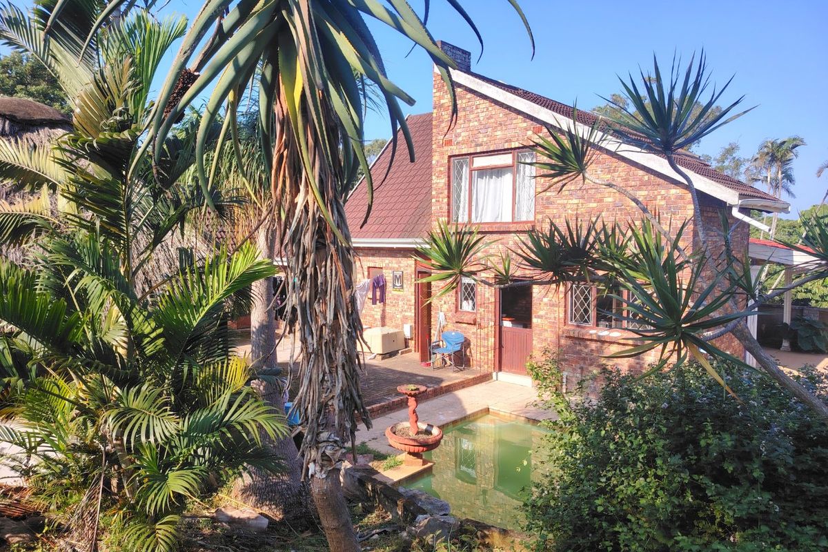 Rear view of a face-brick house featuring a paved patio area and a swimming pool set within a garden.