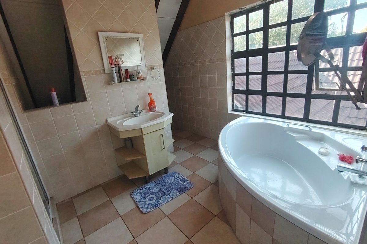 Bathroom featuring a corner bathtub, vanity basin, and tiled finishes with a large grid-pattern window providing natural light.