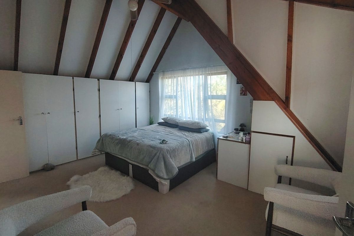 Spacious bedroom featuring exposed timber rafters, a sloped ceiling, built-in cupboards, and a ceiling fan, offering a cozy and character-filled living space.
