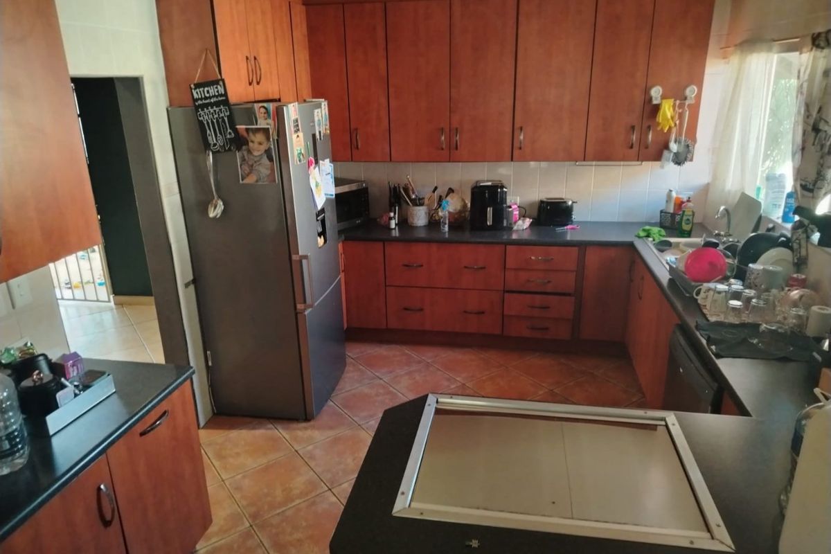 A functional kitchen featuring wood-finish cabinetry, dark laminate countertops, tiled backsplash, and ceramic tile flooring with a practical layout.