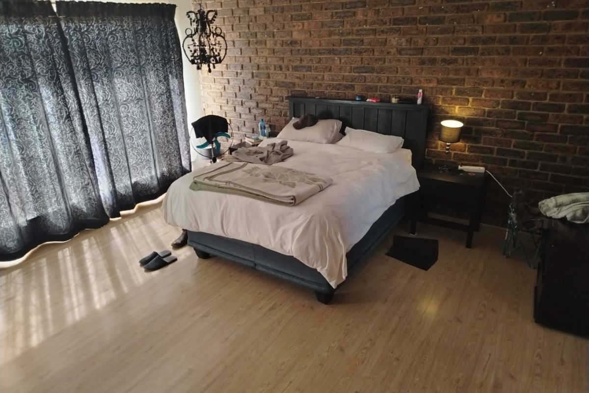 Spacious bedroom featuring a prominent exposed brick feature wall and light-toned laminate flooring, offering a warm and textured aesthetic.