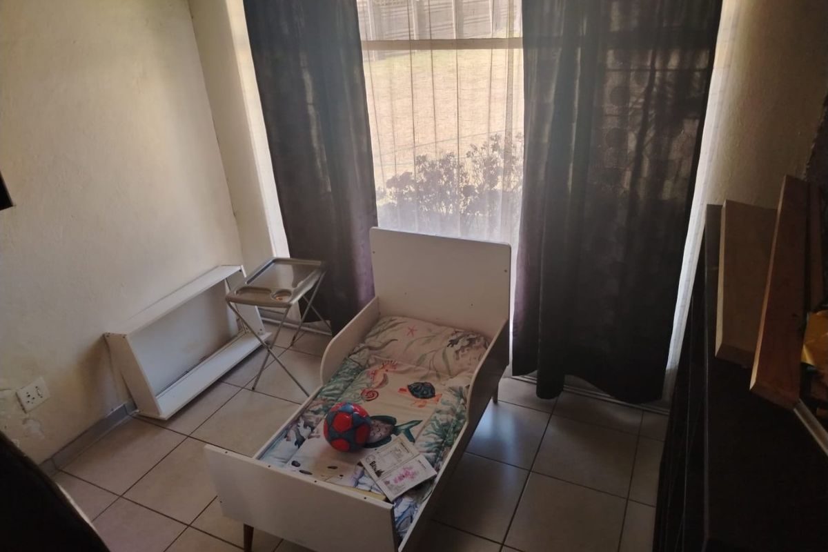 A bedroom featuring tiled flooring and a large window with curtains, providing natural light to the space.