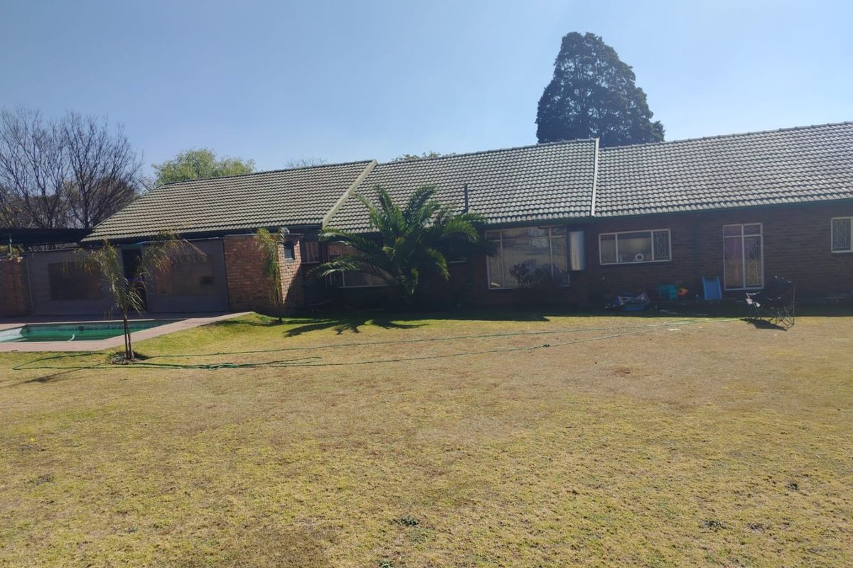 Rear view of the property featuring a brick facade, tiled roof, swimming pool with paved surround, and a spacious lawn area.