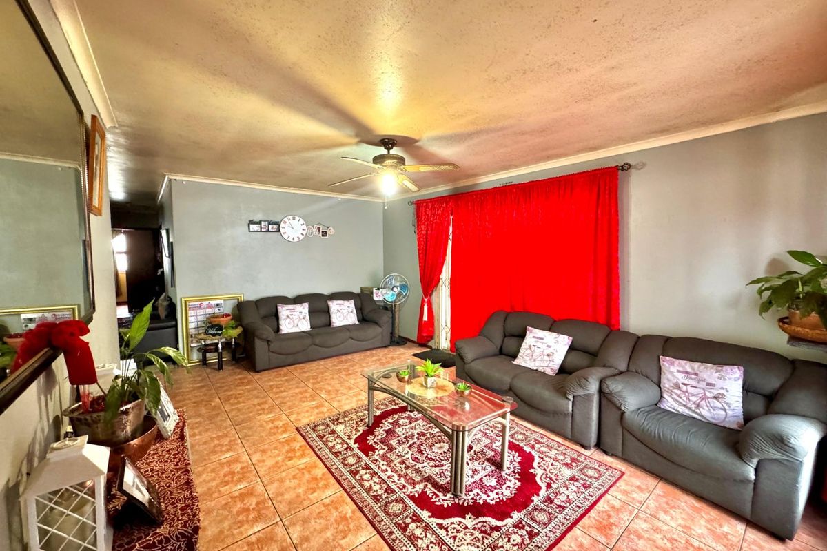 A living room featuring tiled flooring, a ceiling fan, and coved cornicing, currently showing signs of wear on the ceiling.