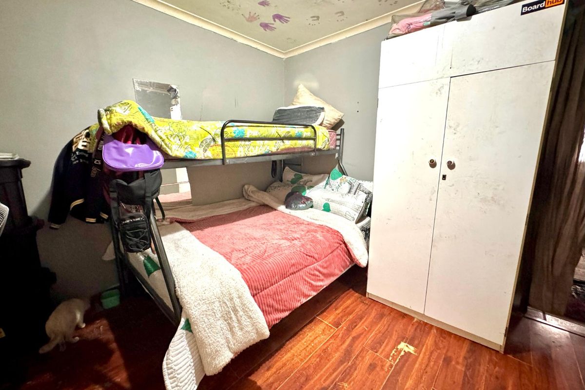 A bedroom featuring laminate flooring and a built-in wardrobe, currently requiring cosmetic updates and repairs to the ceiling and floor surfaces.