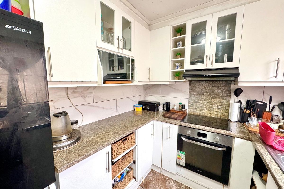 A compact kitchen featuring white cabinetry, laminate countertops, a built-in oven with electric hob, and a tiled backsplash.