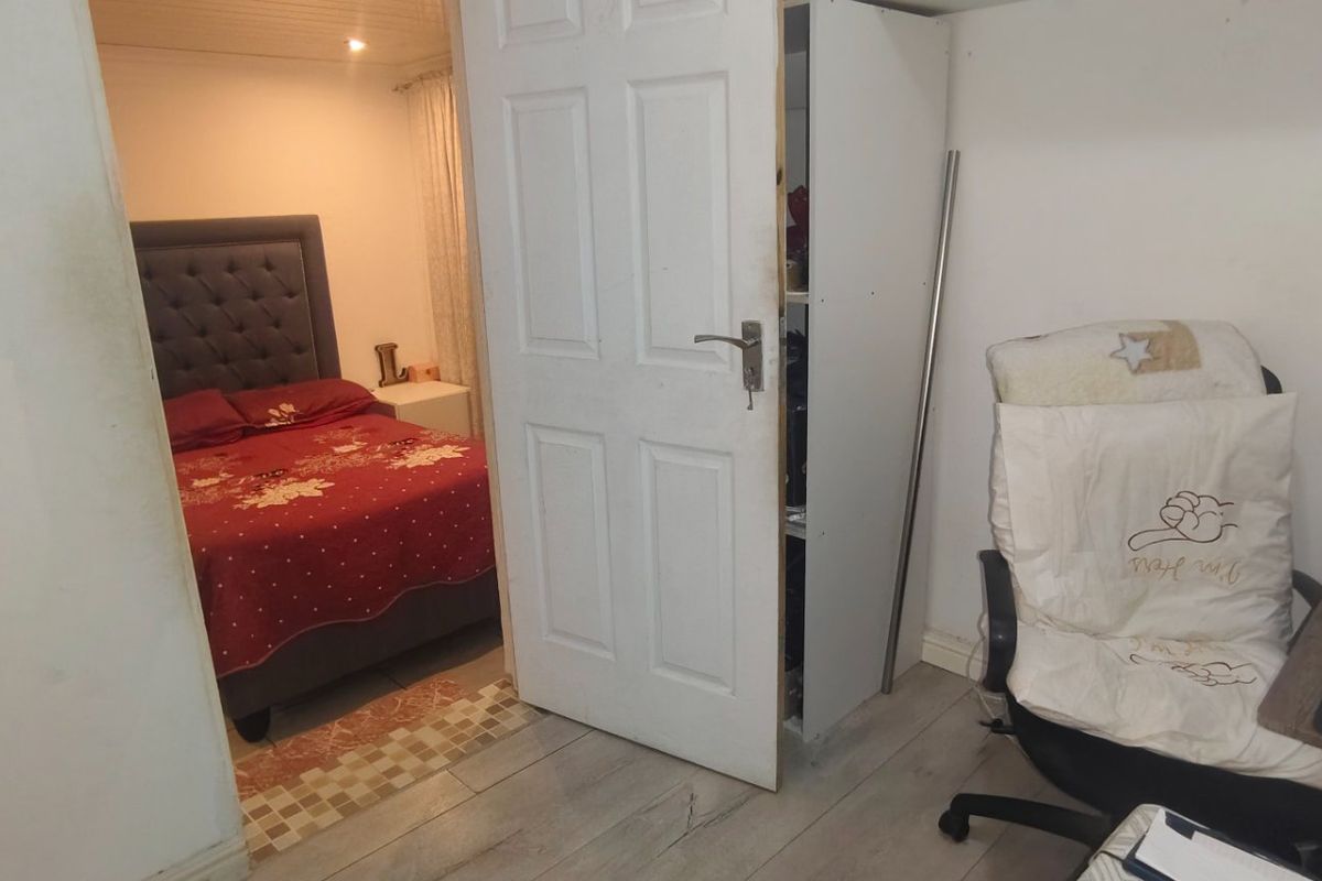 A bedroom interior featuring laminate flooring and a built-in cupboard, showing signs of wear on the walls and door frame.
