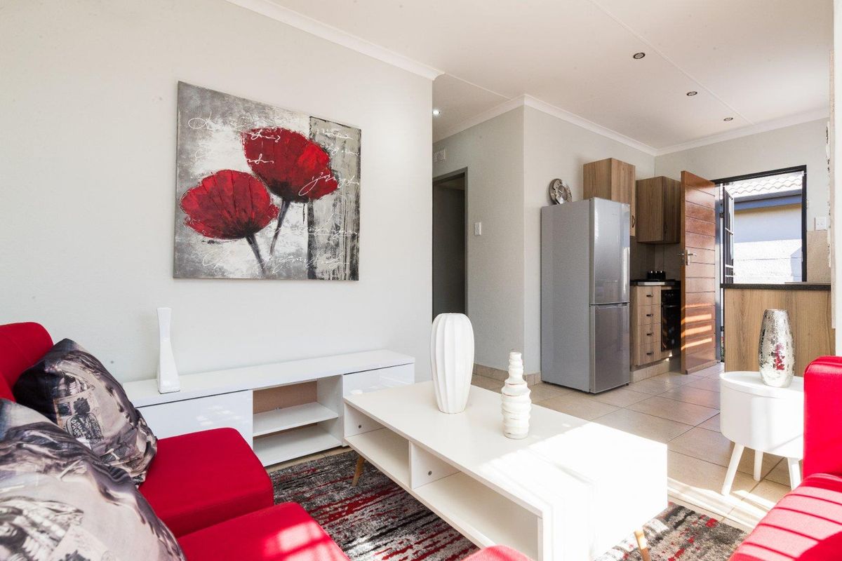 Open-plan living area featuring tiled flooring and recessed lighting, seamlessly connecting to a functional kitchen space with built-in cabinetry and appliances.