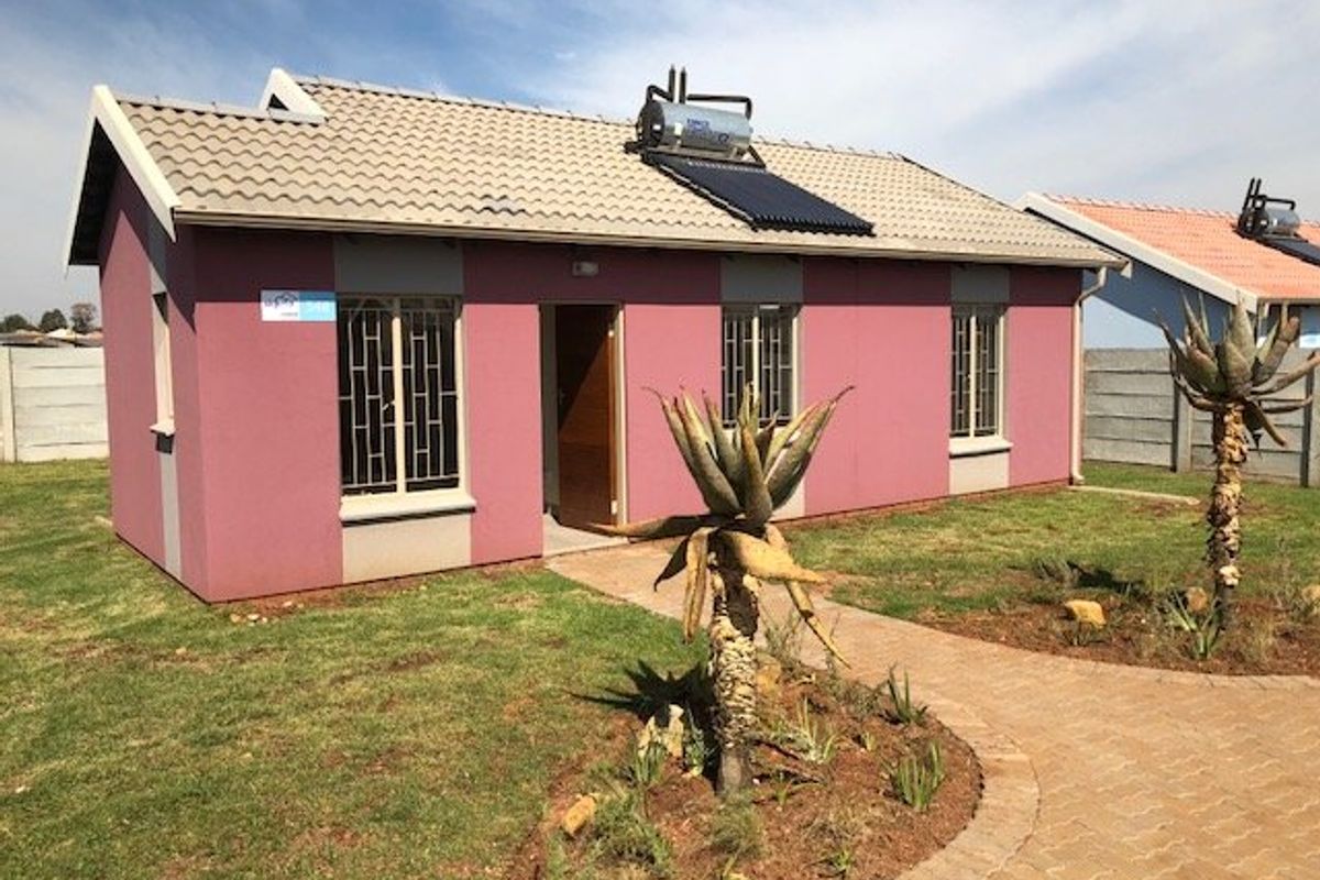 Front view of a detached house featuring a solar water heating system, tiled roof, and a paved walkway leading to the entrance.