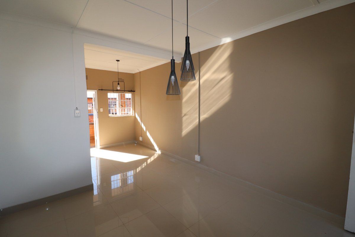 A bright, empty living area featuring polished tiled floors, neutral wall tones, and modern pendant lighting, leading to an exterior access point.