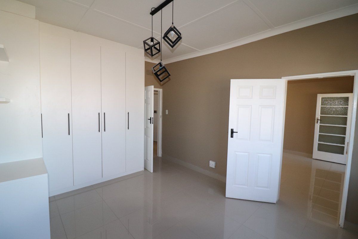 A bright, empty bedroom featuring modern built-in cupboards, neutral tiled flooring, and contemporary pendant lighting, offering a clean and versatile living space.